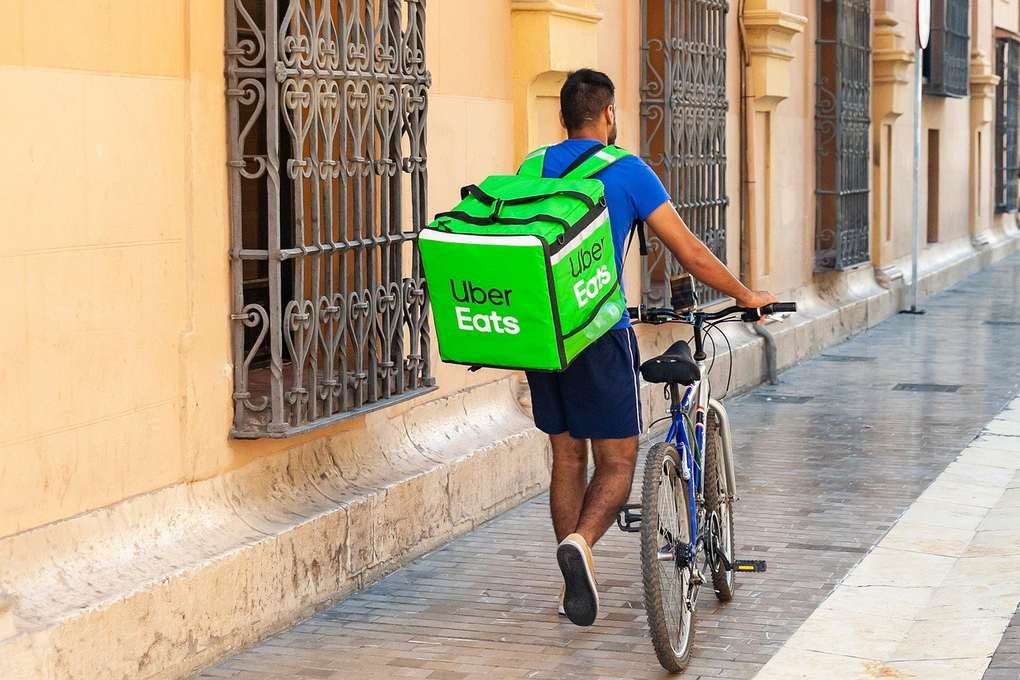 Livreur à vélo portant un sac Uber Eats sur une rue pavée Livreur à vélo portant un sac Uber Eats sur une rue pavée
