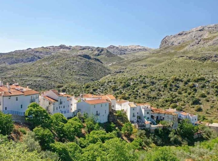 Village blanc aux toits orangés au pied de montagnes boisées sous ciel bleu