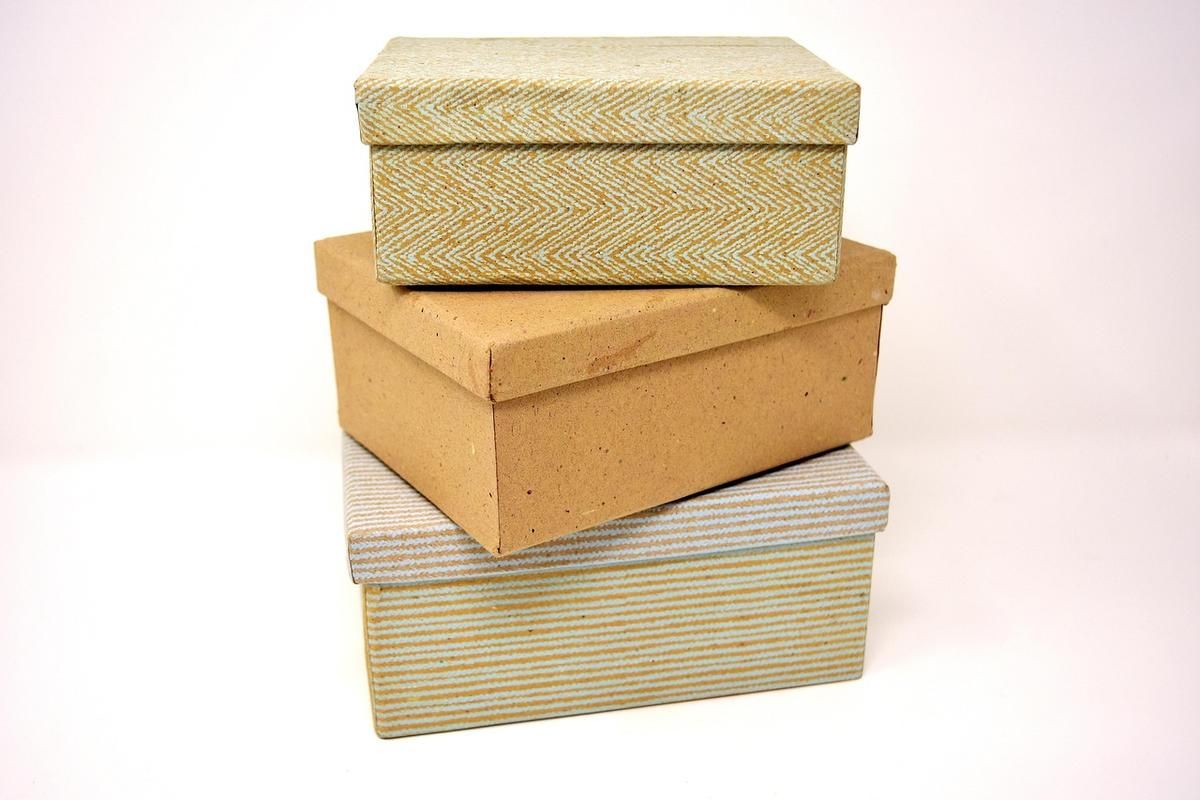 Trois boîtes en carton de différentes textures empilées verticalement sur fond clair