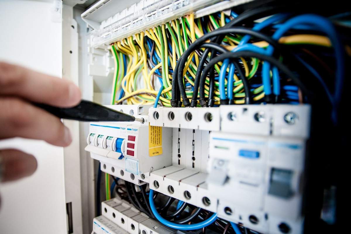 Électroménager ouvert avec fils colorés et interrupteurs, main tenant un outil Électroménager ouvert avec fils colorés et interrupteurs, main tenant un outil