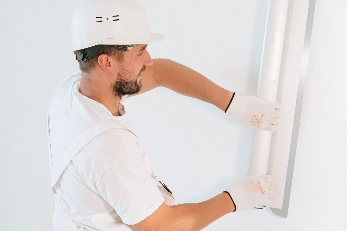 Un ouvrier en tenue blanche installe une plaque sur un mur blanc Un ouvrier en tenue blanche installe une plaque sur un mur blanc
