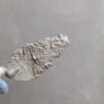 Une main gantée tient une spatule chargée de mortier sur un mur