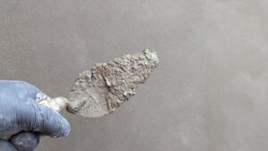 Une main gantée tient une spatule chargée de mortier sur un mur