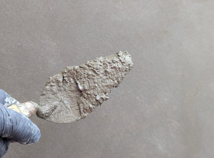 Une main gantée tient une spatule chargée de mortier sur un mur